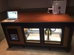 an open laptop computer sitting on top of a wooden table next to a small refrigerator