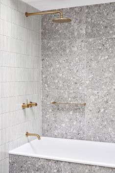 a white bath tub sitting next to a wall with gold faucets on it