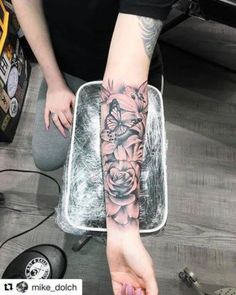 a person with a tattoo on their arm holding a glass container filled with flowers and butterflies