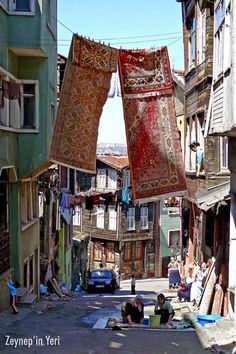 two people are sitting on the ground in an alleyway with clothes hanging above them