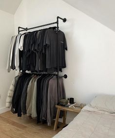 there is a rack with clothes on it in the corner next to a bed and a small table