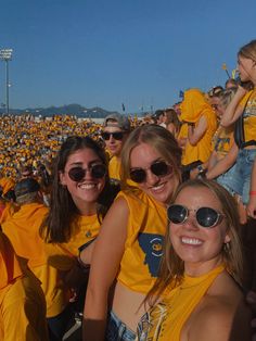 a group of people in yellow shirts and sunglasses at a sporting event with one person taking a selfie