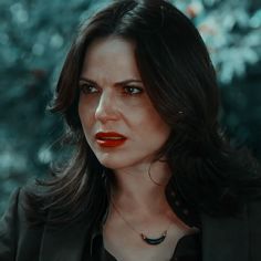 a woman with dark hair wearing a black jacket and red lipstick looks at the camera