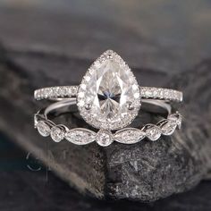 an engagement ring with a pear shaped diamond in the center on top of a rock