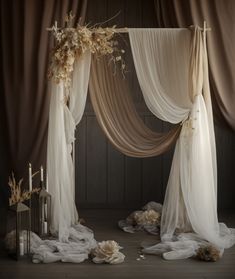 a white wedding arch with sheer drapes and flowers on the floor in front of it