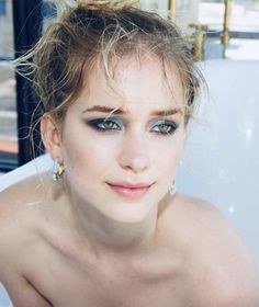 a beautiful young woman sitting in a bathtub with blue eyeshadow and gold hoop earrings