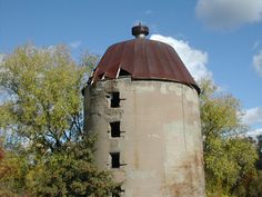 an old tower with a rusted metal roof sits in front of trees and clouds