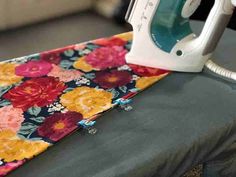 an iron is sitting on top of a flowered cloth next to the ironing board