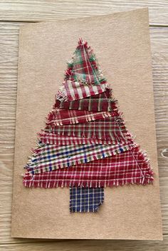 a christmas tree made out of fabric on top of a piece of brown paper with red, white and blue plaid ribbon