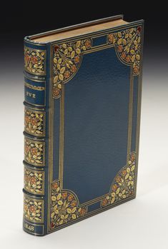 a blue book with gold trimmings and flowers on the cover, sitting on a white surface