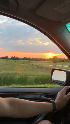 a person driving a car with the sun setting in the background and grass on the ground