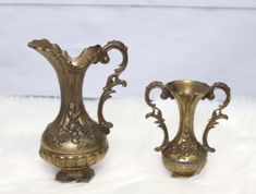 two brass vases sitting on top of a white furnishing covered floor next to each other