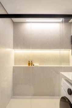 a washer sitting next to a dryer in a white tiled room with glass walls