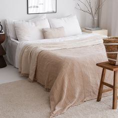 a bed with white linens and pillows in a bedroom next to a wooden chair