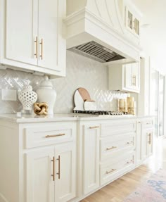 a kitchen with white cabinets and gold trim on the counter tops, along with an oven hood