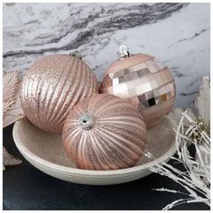 three shiny pink ornaments in a bowl on a marble counter top with white and black accents