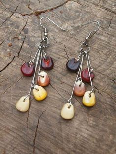 three pairs of earrings with dangling hooks on wooden table next to tree trunk and rock