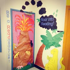 two doors decorated with dinosaurs and palm trees in front of a bulletin board that says roar into reading