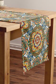 a wooden table topped with a colorfully patterned table runner next to a cup and saucer