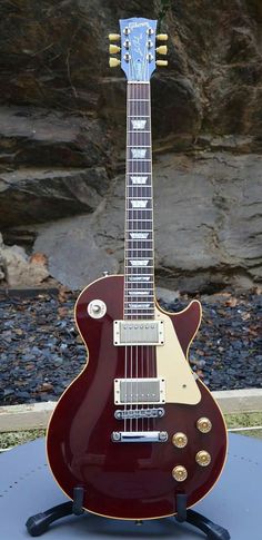 a red electric guitar sitting on top of a blue table next to a rock wall