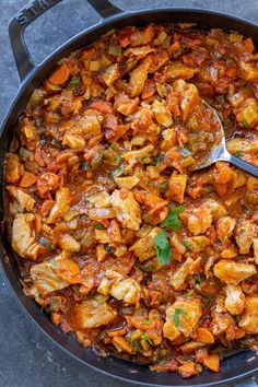 a skillet filled with chicken and vegetables on top of a table next to a spoon