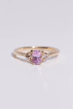 a yellow gold ring with an oval shaped pink sapphire and three small diamonds on the side