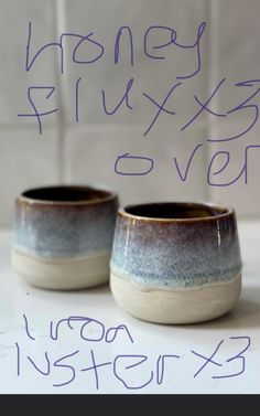 two ceramic cups sitting on top of a counter next to a sign that says honey gluxers oven