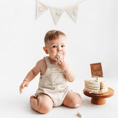 a baby sitting on the floor with cake in front of him and holding his hand up to his mouth