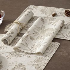 two placemats on a table with pine cones and fruit in a bowl next to them