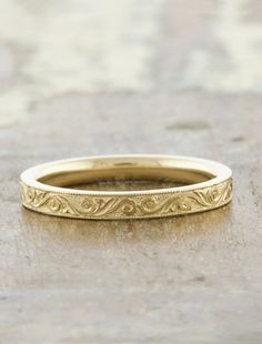 a gold wedding band with intricate designs on the outside and inside, sitting on a stone surface