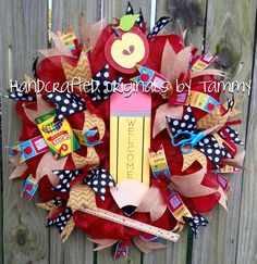 a red mesh wreath with an apple and pencil on it, sitting next to a fence