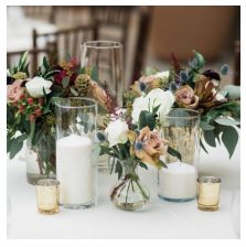 three vases filled with flowers and candles sitting on top of a white table cloth