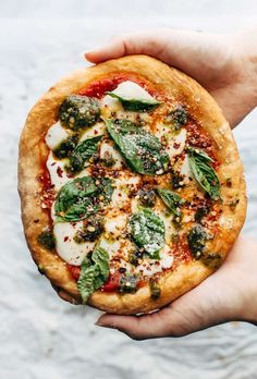 a person holding a small pizza with cheese and spinach on it's crust