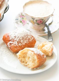 powdered sugar covered pastries on a plate next to a cup and saucer