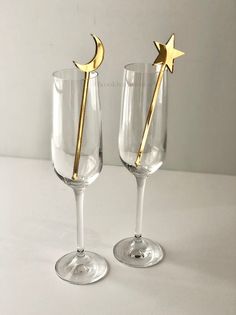 two wine glasses with gold stars and a crescent on the top one has a toothpick in it