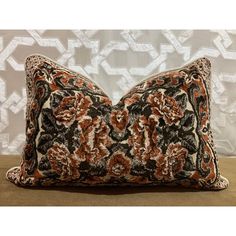 an orange, black and white pillow on a wooden table next to a decorative wall