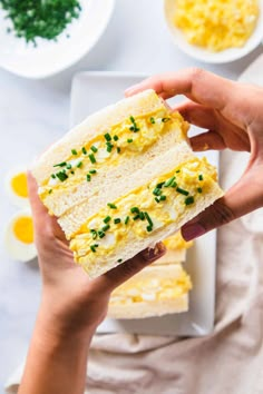 someone holding up a piece of bread with eggs and chives on it in front of other plates