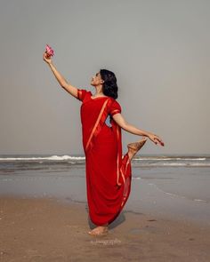 a woman in a red sari on the beach with her arms outstretched up to catch a frisbee