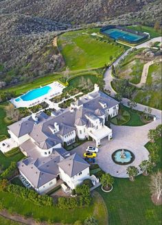 an aerial view of a large white mansion with a pool in the middle and lots of greenery surrounding it