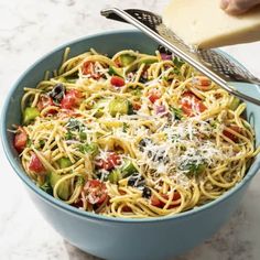 a blue bowl filled with pasta and veggies next to a piece of bread