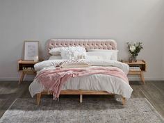 a bed with white and pink linens in a bedroom next to a wooden table