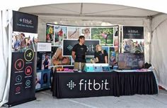 a man standing in front of a fitbit booth at an outdoor event with posters on the wall