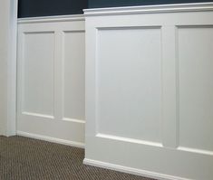 an empty room with white paneling on the walls and carpeted floor, in front of a blue wall