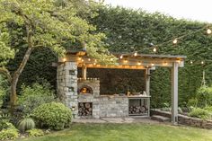 an outdoor bbq with lights strung from the roof and trees in the back ground