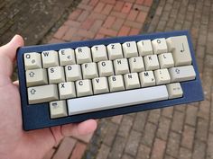 a hand is holding a computer keyboard on brick pavemented area with cobblestones