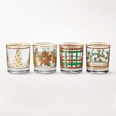 four glass tumblers decorated with christmas designs and decorations, all lined up against a white background