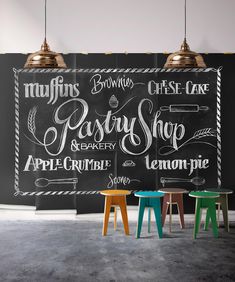 three stools in front of a chalkboard with writing on it and two lamps hanging from the ceiling