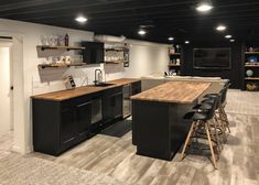 a kitchen with black cabinets and wooden counter tops next to an open floor plan area