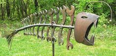 a large metal fish sculpture sitting on top of a lush green field