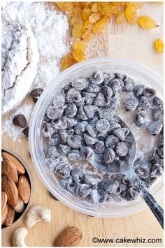 a bowl filled with nuts and raisins on top of a wooden table next to a spoon